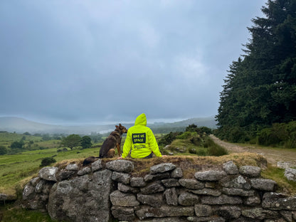 owner-wearing-hi-vis-training-hoodie-and-nervous-dog-sitting-on-rock-wall-overseeing-landscape