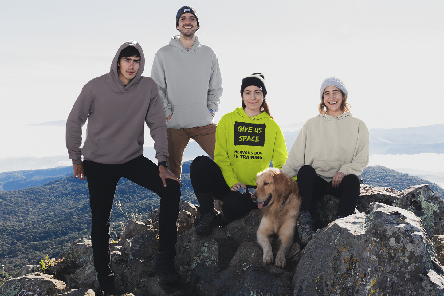 group-of-friends-posing-at-the-top-of-a-hill-with-lady-in-the-middle-wearing-bright-yellow-nervous-dog-in-training-hoodie-sat-on-the-rocks-with-her-golden-retriever-dog